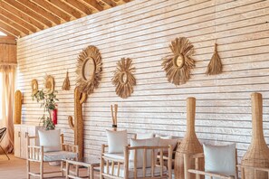Una habitación con paredes de listones de madera, múltiples adornos tejidos en las paredes y una zona de estar con sillas acolchadas y una mesa de madera.