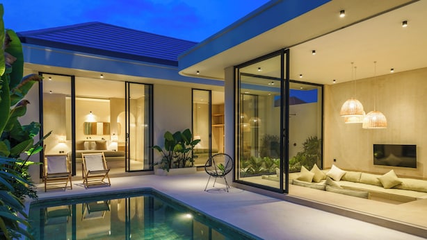 Una casa moderna con piscina, puertas de cristal y una sala de estar con sofá y sillones.