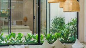 Una sala de estar moderna con un sofá seccional grande, una mesa de centro de madera y un ventanal de vidrio que da a un balcón con plantas.