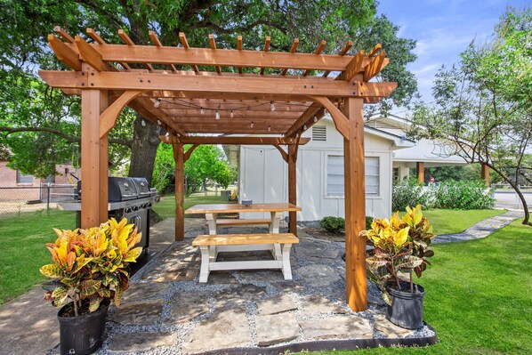 Relax on a bench beneath a charming pergola, surrounded by lush greenery and a beautifully manicured lawn.