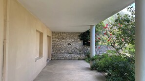 Un espace extérieur abrité, doté d’un mur en pierre, d’un sol en béton et de verdure.