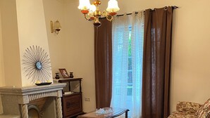 Un soggiorno con camino, un lampadario, due poltrone, un tavolino da caffè e un tappeto decorato.