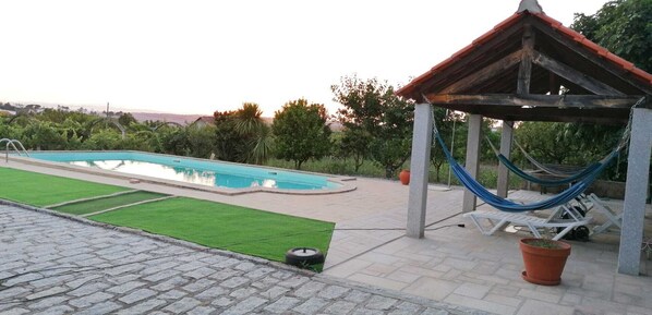 Una piscina con un patio circundante, una hamaca y un pequeño pabellón.