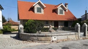 Una casa a due piani con tetto in tegole rosse, pareti in pietra e una recinzione in pietra.