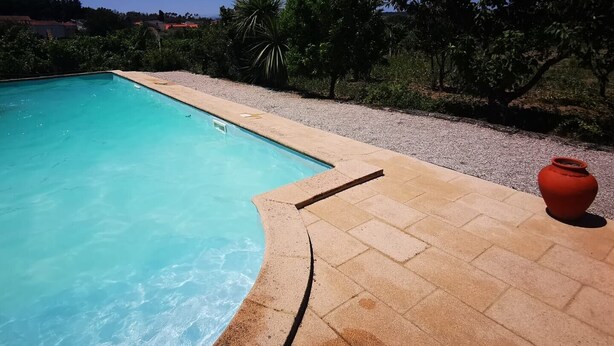 Una piscina con acqua cristallina, circondata da un vialetto di ciottoli e vegetazione.