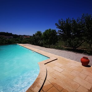 Una piscina con agua cristalina azul, rodeada de un sendero de piedrecitas y vegetación.