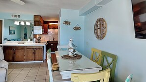 Un coin repas avec une table et des chaises, une cuisine en arrière-plan et des horloges décoratives au mur.