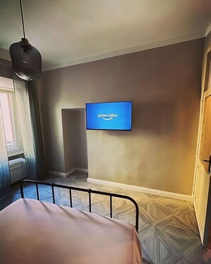 A bedroom with a bed, a television mounted on the wall displaying the Prime Video logo, a window with blinds, and a door. - Come discover the charms of Tivoli at Casetta Beatrice! (Tivoli)