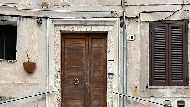 Un edificio con puerta de madera, escalones de piedra y un cartel con el número 20.