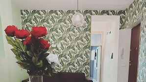 Una zona de comedor con una mesa de madera, un jarrón de flores rojas, una computadora portátil y un croissant sobre la mesa.