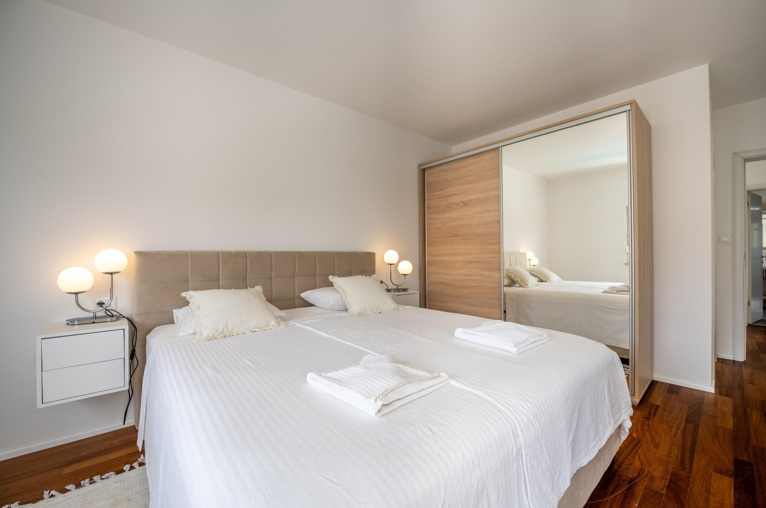 Quarto moderno com uma cama grande, luminárias de cabeceira, um espelho e piso de madeira.