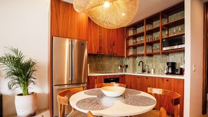 Een moderne keuken met houten kastjes, een roestvrijstalen koelkast, een ronde eettafel met geweven placematen, en een potplant.