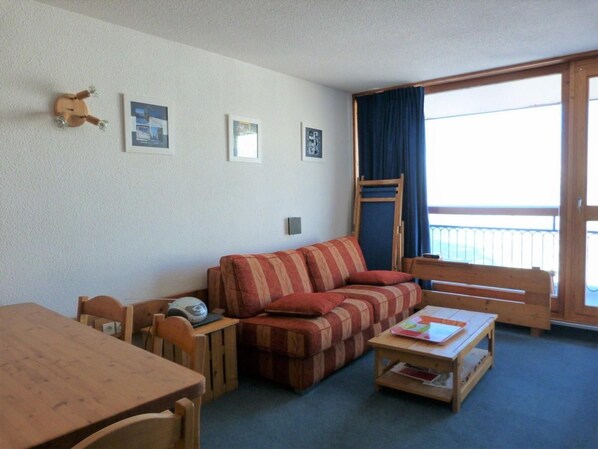 A furnished room with a sofa, a table, chairs, a wooden bench, and a window with a view.