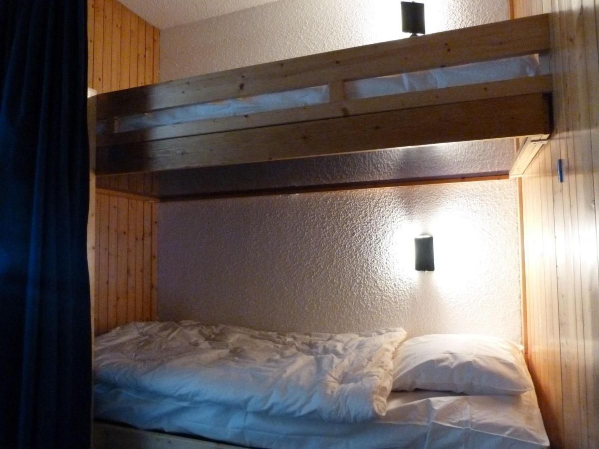 A bunk bed with a wooden headboard, a single bed below, and a wall-mounted light fixture.