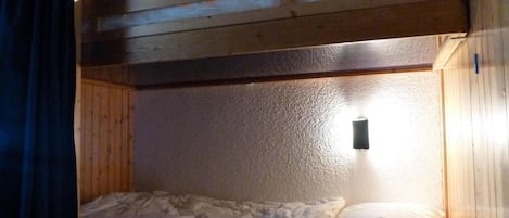 A bunk bed with a wooden headboard, a single bed below, and a wall-mounted light fixture.