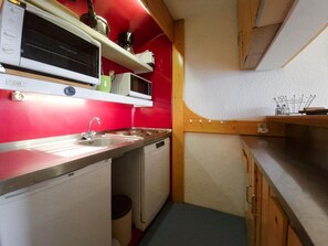 A compact kitchenette with a microwave, stove, sink, and storage cabinets.