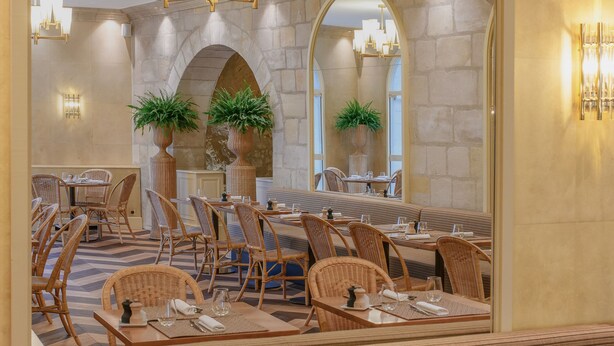 A restaurant with a stone wall, arched ceiling, wicker furniture, and potted plants. - Les Hautes Roches (Rochecorbon)