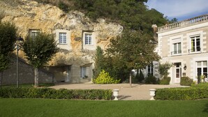 A building with a stone facade, a garden with a lawn and a few trees, and a clear sky. - Les Hautes Roches (Rochecorbon)
