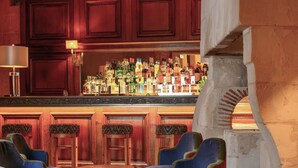 A bar area with wooden paneling, a variety of liquor bottles, and several blue upholstered chairs and round wooden tables. - Les Hautes Roches (Rochecorbon)
