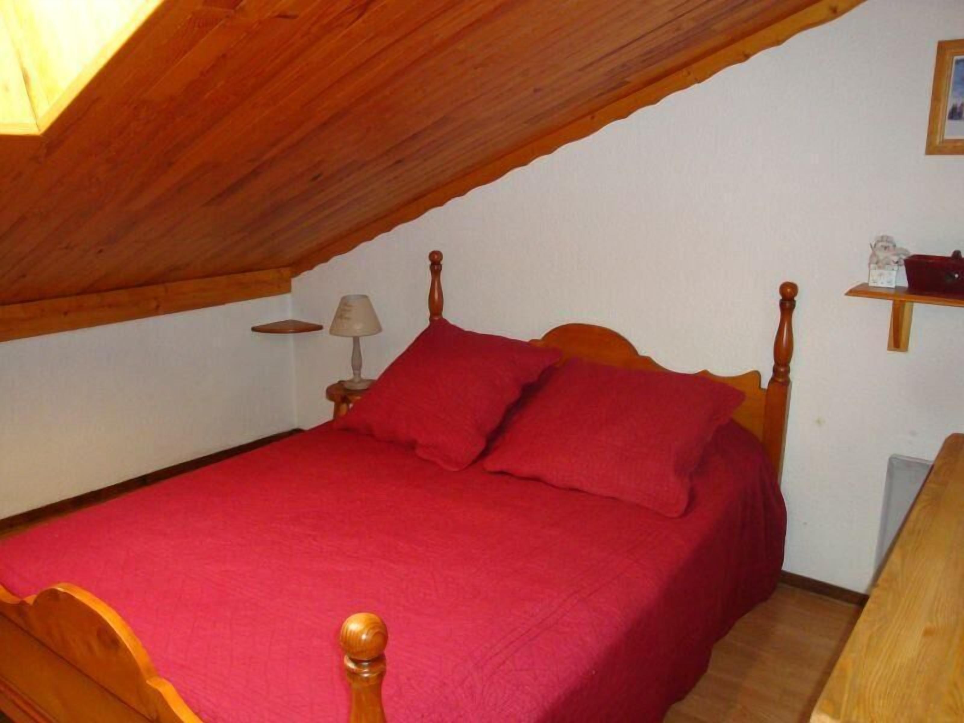 Un lit simple dans une chambre dont le plafond est en pente, une table de chevet avec une lampe et une petite étagère avec quelques objets.