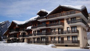 Un hotel de varios pisos con balcones, con una imponente montaña nevada al fondo.