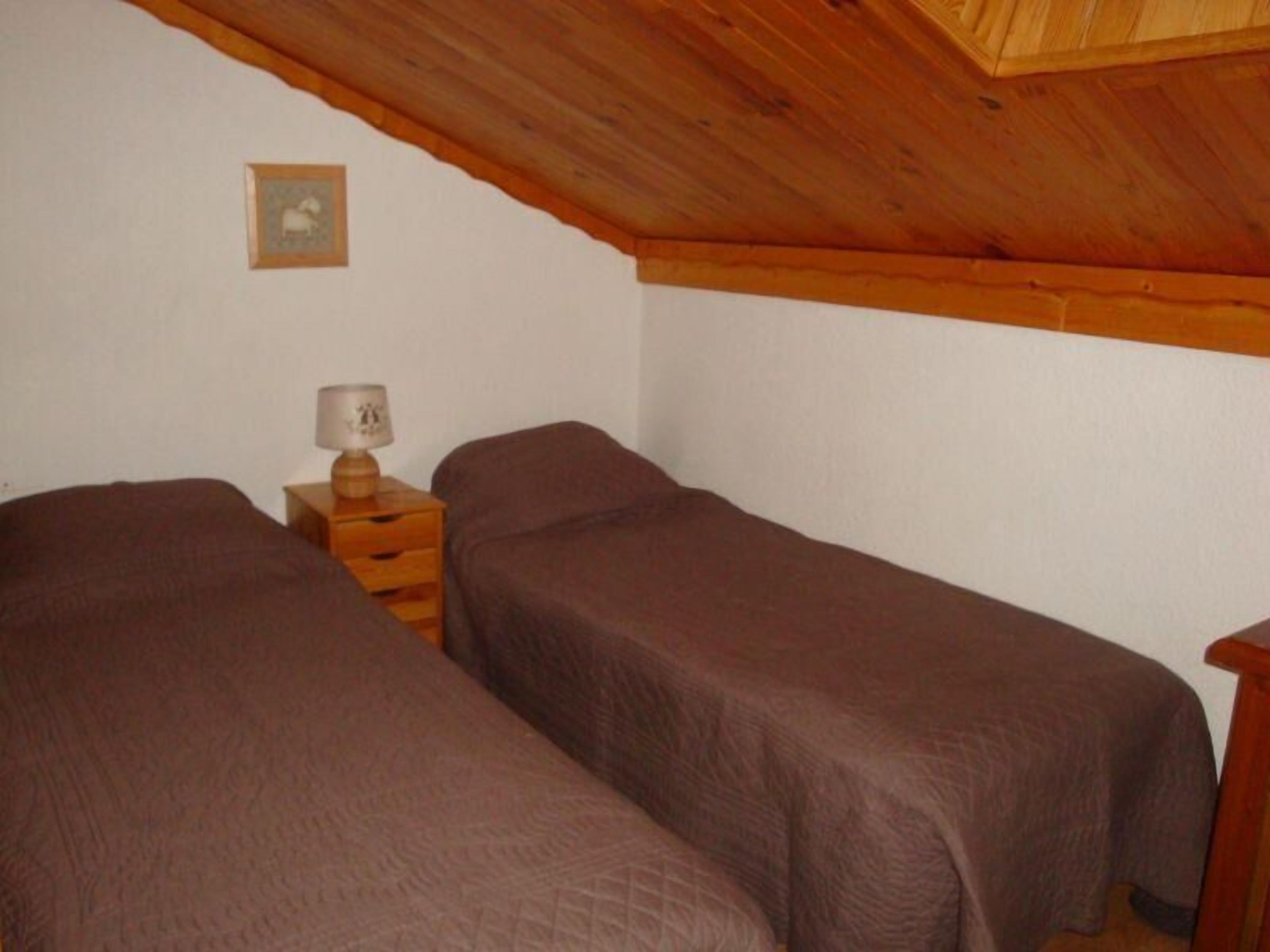 Une petite chambre agréable, dotée de deux lits simples, d’une table de chevet en bois avec une lampe et d’un tableau encadré au mur.