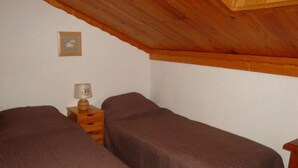 Una habitación pequeña y acogedora con dos camas individuales, una mesita de noche de madera con una lámpara y un cuadro en la pared.