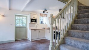 A kitchen with white cabinets, a microwave, and a window. - The Stables - 2 Bedroom Cottage - Princes Gate (Narberth)