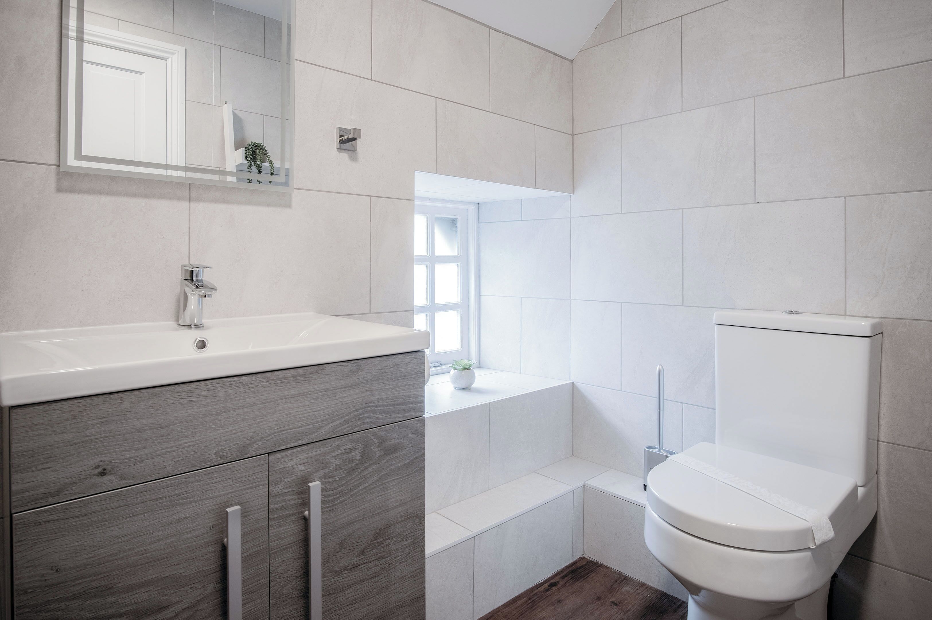 Un baño moderno con un lavabo blanco, tocador de madera y un inodoro.