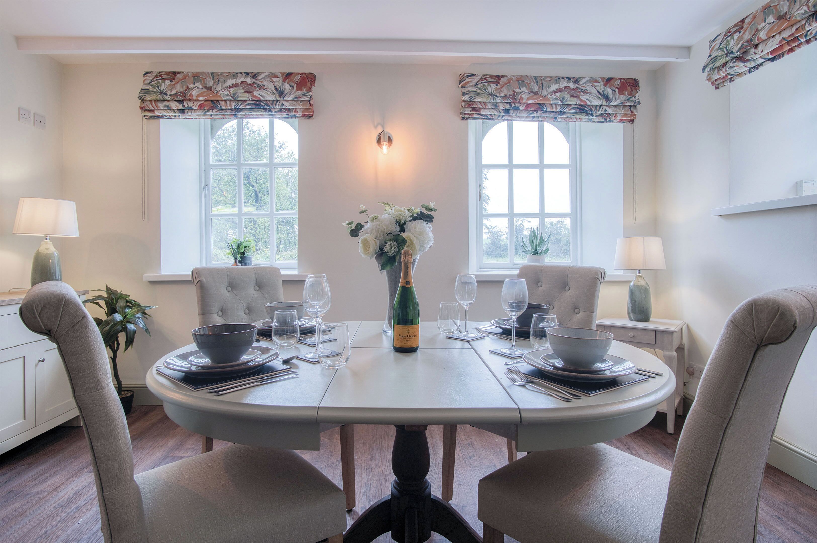 A dining table set for two with a bottle of champagne, two chairs, and a vase of flowers.