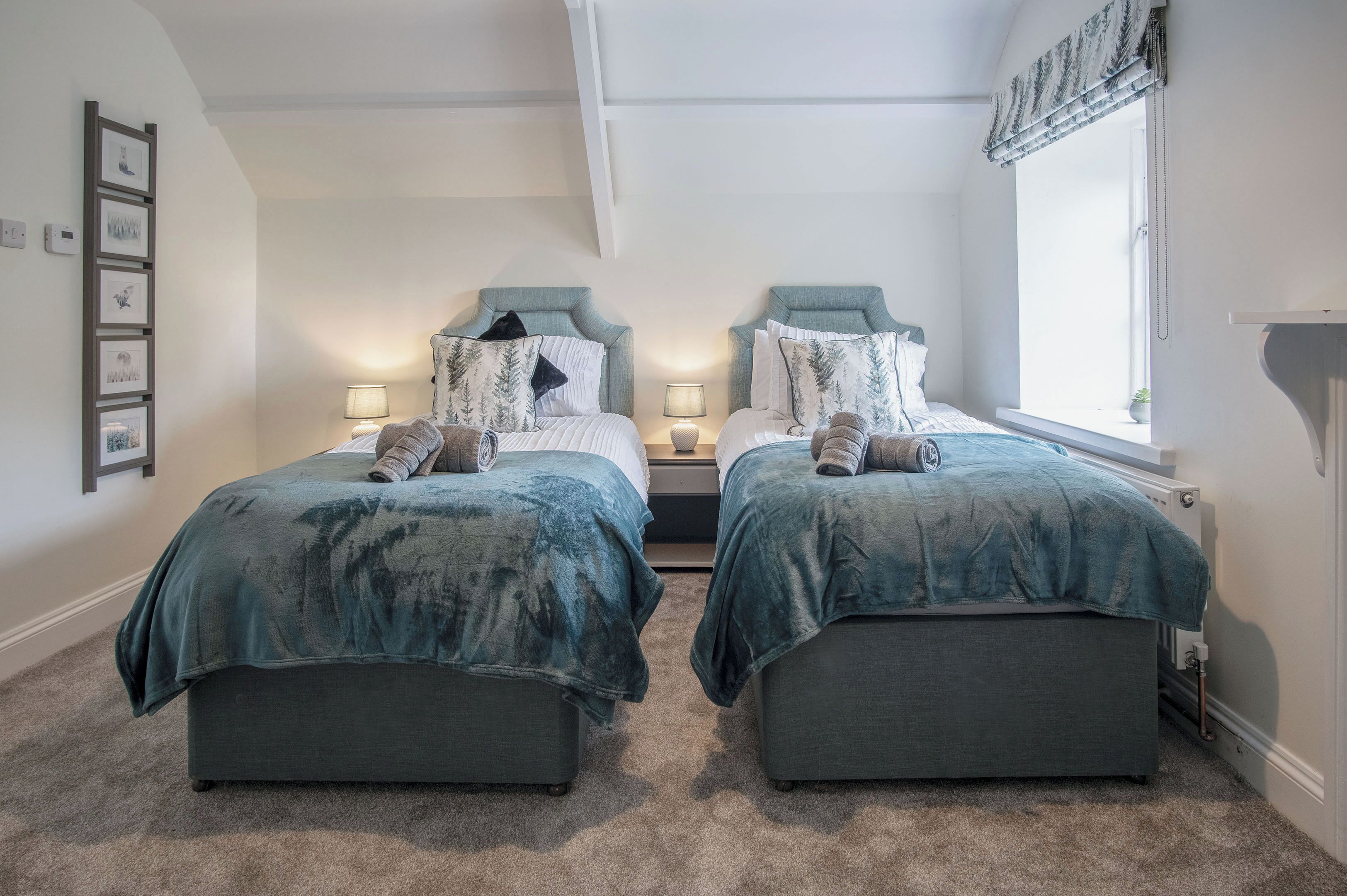 A bedroom with two beds, each with a headboard, bedside tables, and lamps. There is a window with a view of the outside.