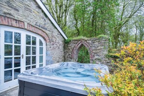 A stone building with a large window and a hot tub in front. - The Stables - 2 Bedroom Cottage - Princes Gate (Narberth)