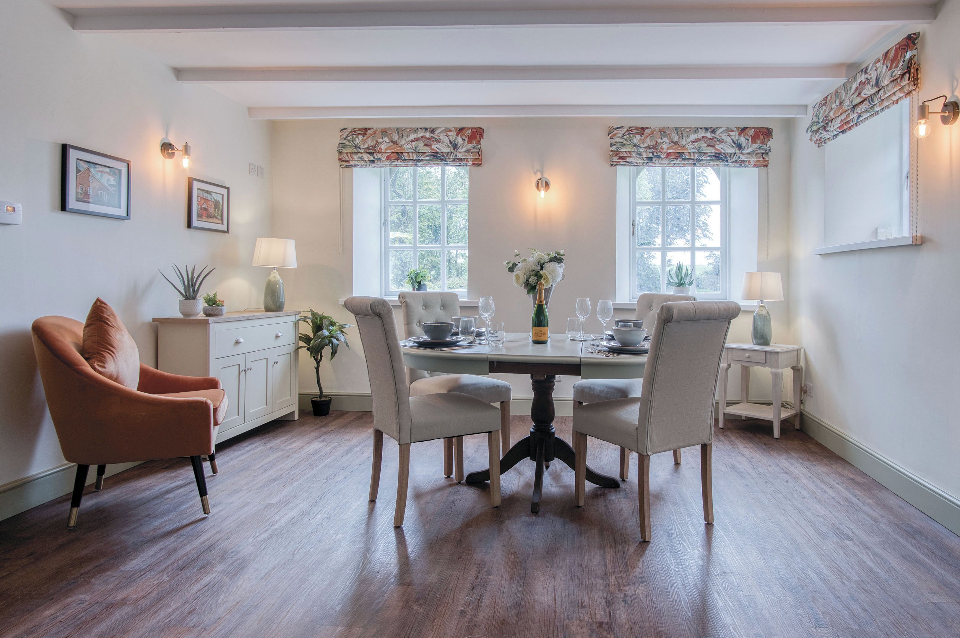 Un coin repas comprenant une table ronde, quatre chaises, un vase de fleurs et deux lampes.