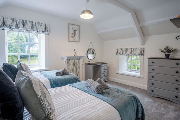 A bedroom with two beds, a dresser, a mirror, and a fireplace. - The Stables - 2 Bedroom Cottage - Princes Gate (Narberth)