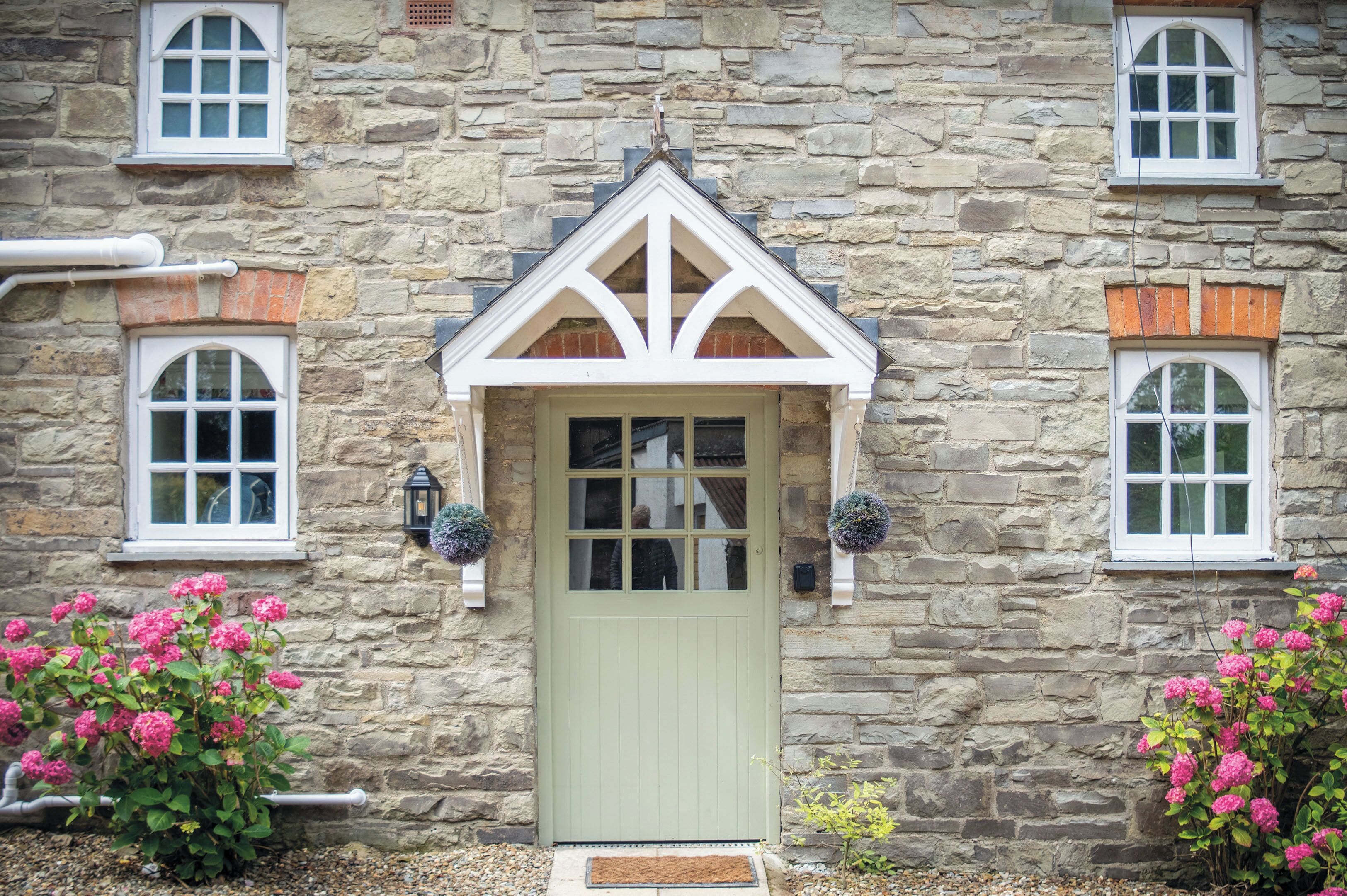 A stone building with a green door, white windows, and a triangular gable.