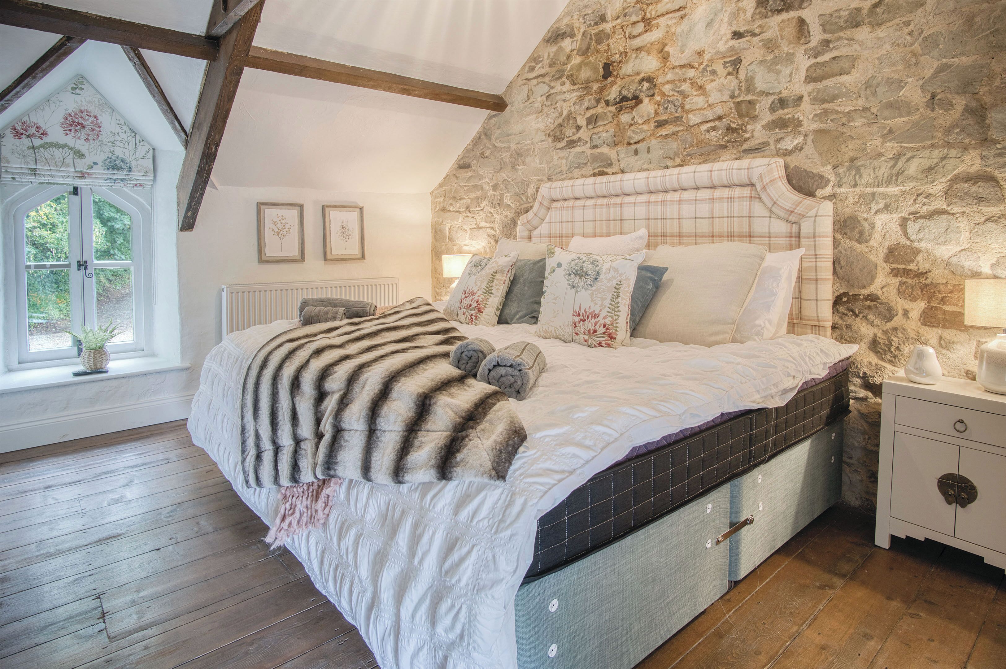 Une chambre avec un mur en pierre, un lit avec une couette, des oreillers et une table de chevet.