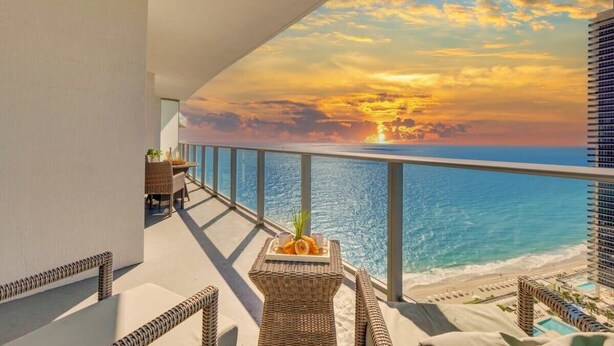 Un balcone con vista sull'oceano e sul tramonto, arredato con mobili in vimini e un vassoio con degli snack.