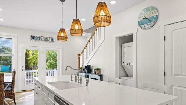 A modern kitchen with a large island, pendant lights, and a clock on the wall. - High Tide Hideaway by Seaside Vacations & Sales (Chincoteague Island)