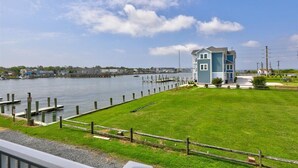 A waterfront property with a dock, a grassy lawn, and a blue building with a sloped roof. - No Problem (Formerly The Teague House) by Seaside Vacations & Sales (Chincoteague Island)