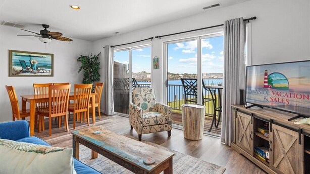 A spacious living room with a balcony, wooden furniture, a television, and a view of the sea. - No Problem (Formerly The Teague House) by Seaside Vacations & Sales (Chincoteague Island)