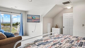A bedroom with a bed, a window with a view, a TV, and a door. - No Problem (Formerly The Teague House) by Seaside Vacations & Sales (Chincoteague Island)