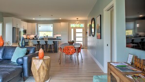 A modern kitchen with white cabinets, a dining area with orange chairs, and a living room with a dark sofa and a wooden coffee table. - Hops and Dreams by Carolina Mornings | Hot Tub, Mtn Views⛰️+Biltmore Pass (Leicester)