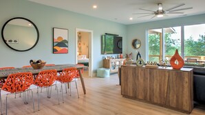 A modern dining area with a wooden table and orange chairs, a wooden cabinet with decorative items, and a large mirror on the wall. - Hops and Dreams by Carolina Mornings | Hot Tub, Mtn Views⛰️+Biltmore Pass (Leicester)
