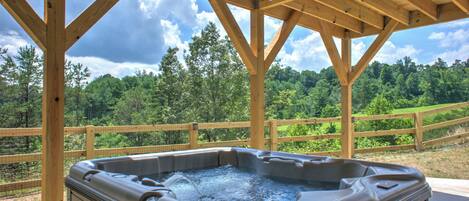 A hot tub under a wooden pergola with a view of a forested area.