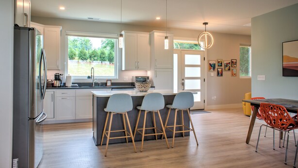 A modern kitchen with a central island, bar stools, and a dining area with a table and chairs. - Hops and Dreams by Carolina Mornings | Hot Tub, Mtn Views⛰️+Biltmore Pass (Leicester)