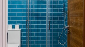 Une salle de bain avec une douche à parois de verre, des toilettes blanches et des murs recouverts de carreaux bleus.