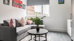 Un salon moderne avec un canapé gris, une petite table ronde ornée d’une plante et des œuvres d’art accrochées aux murs.