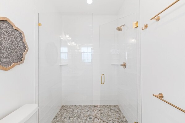 A modern bathroom with a glass shower enclosure, a white toilet, and a decorative wall piece. - Knee Deep: 4 Bedrooms, Private Pool, Close to Restaurants (St. George IUsland)