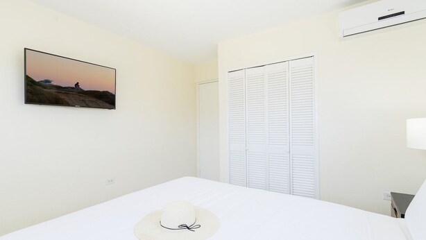 A hotel room with a bed, a wall-mounted TV, a white closet, and a white hat on the bed. - Luxury 6BR Villa w/ Private Pool near Palm Beach (Noord)