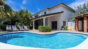 A modern house with a swimming pool, a covered patio, and a garden with palm trees.